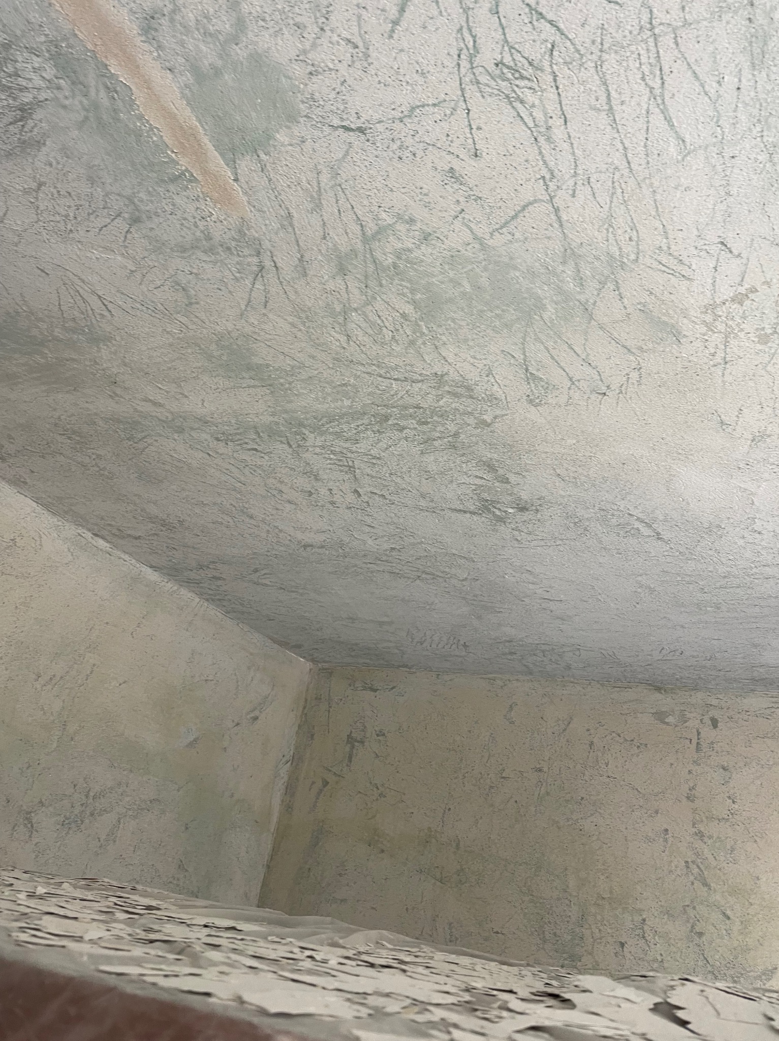 Przygotowana do malowania ściana z widocznymi śladami szpachlowania i rysami na suficie, surowy stan wykończenia wnętrza.