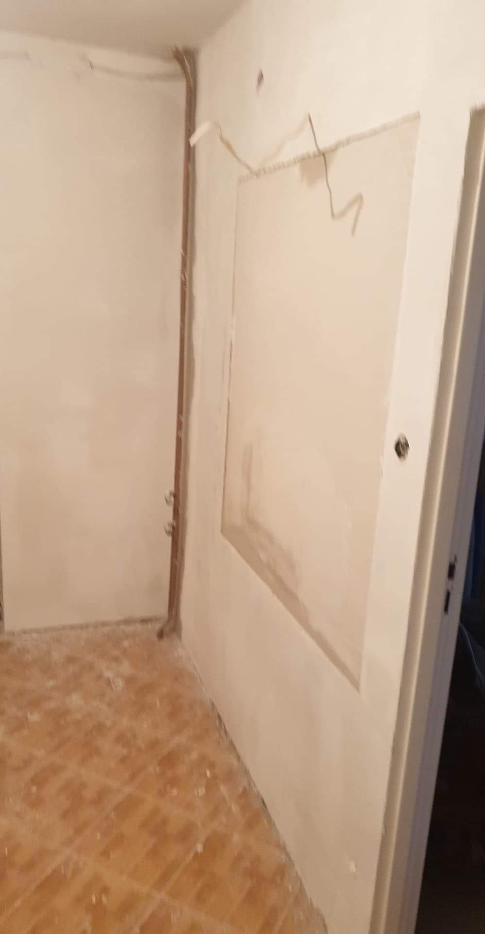 Wnętrze w trakcie remontu: przygotowana ściana z widocznymi przewodami elektrycznymi, częściowo zagruntowana pod gładzie, z widocznym fragmentem starej instalacji elektrycznej i fragmentem podłogi...