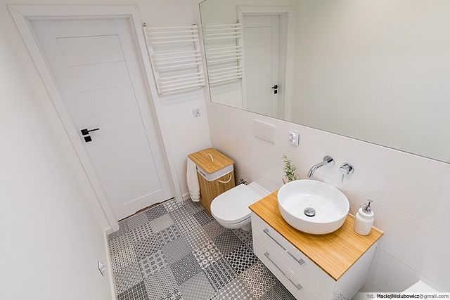 Nowoczesna łazienka z patchworkową podłogą, białą umywalką nablatową na szafce z bambusowym blatem, wiszącą toaletą i bambusowym koszem na pranie.