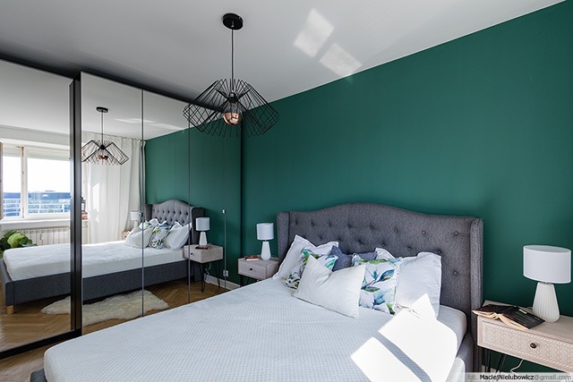 Sypialnia z łóżkiem o szarym wezgłowiu, zieloną ścianą, nowoczesną lampą wiszącą i szafą z lustrzanymi drzwiami.