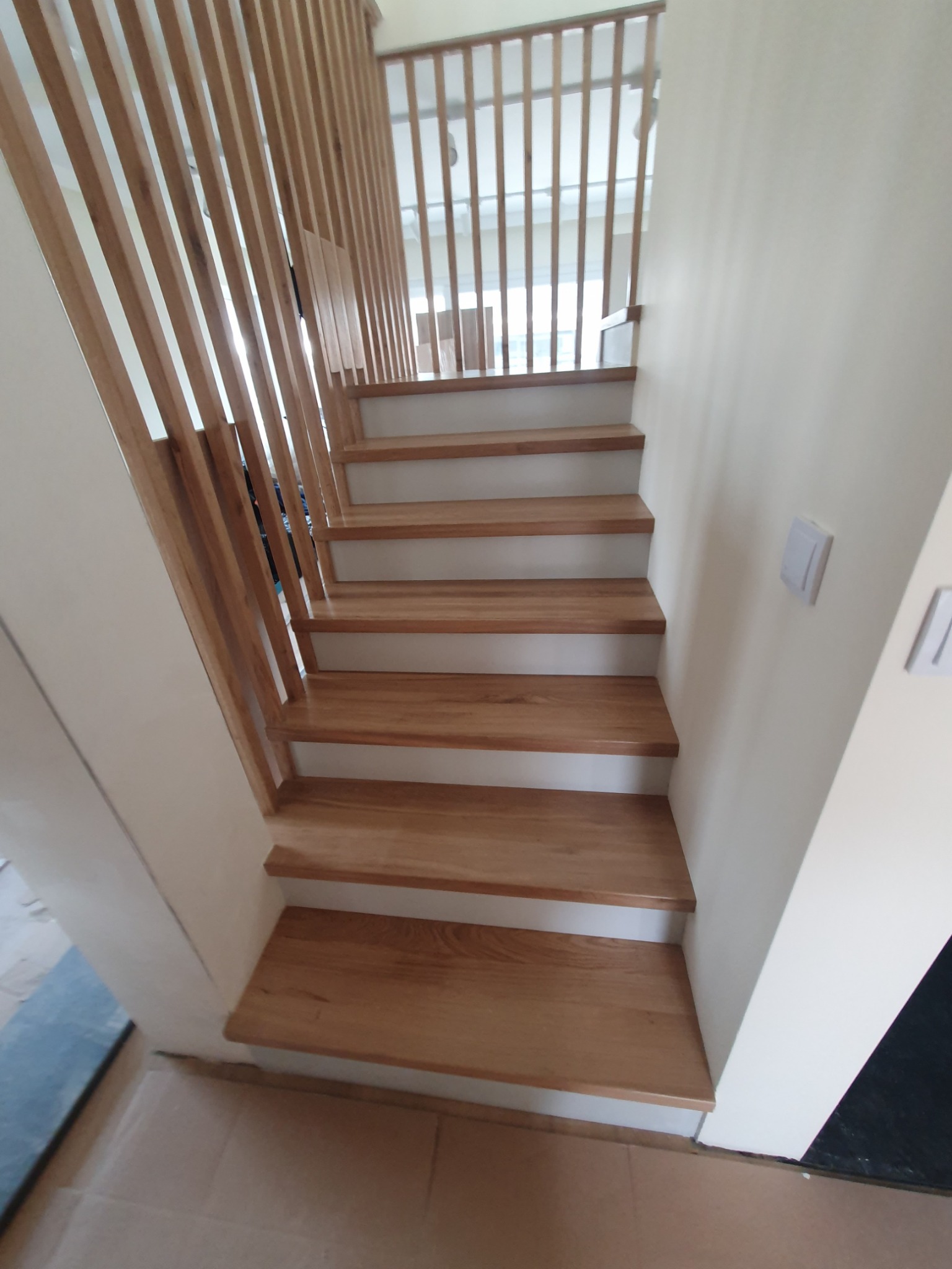 Bieg schodów z jasnego drewna z pionową balustradą z listewek, widok z dołu, minimalistyczny design.