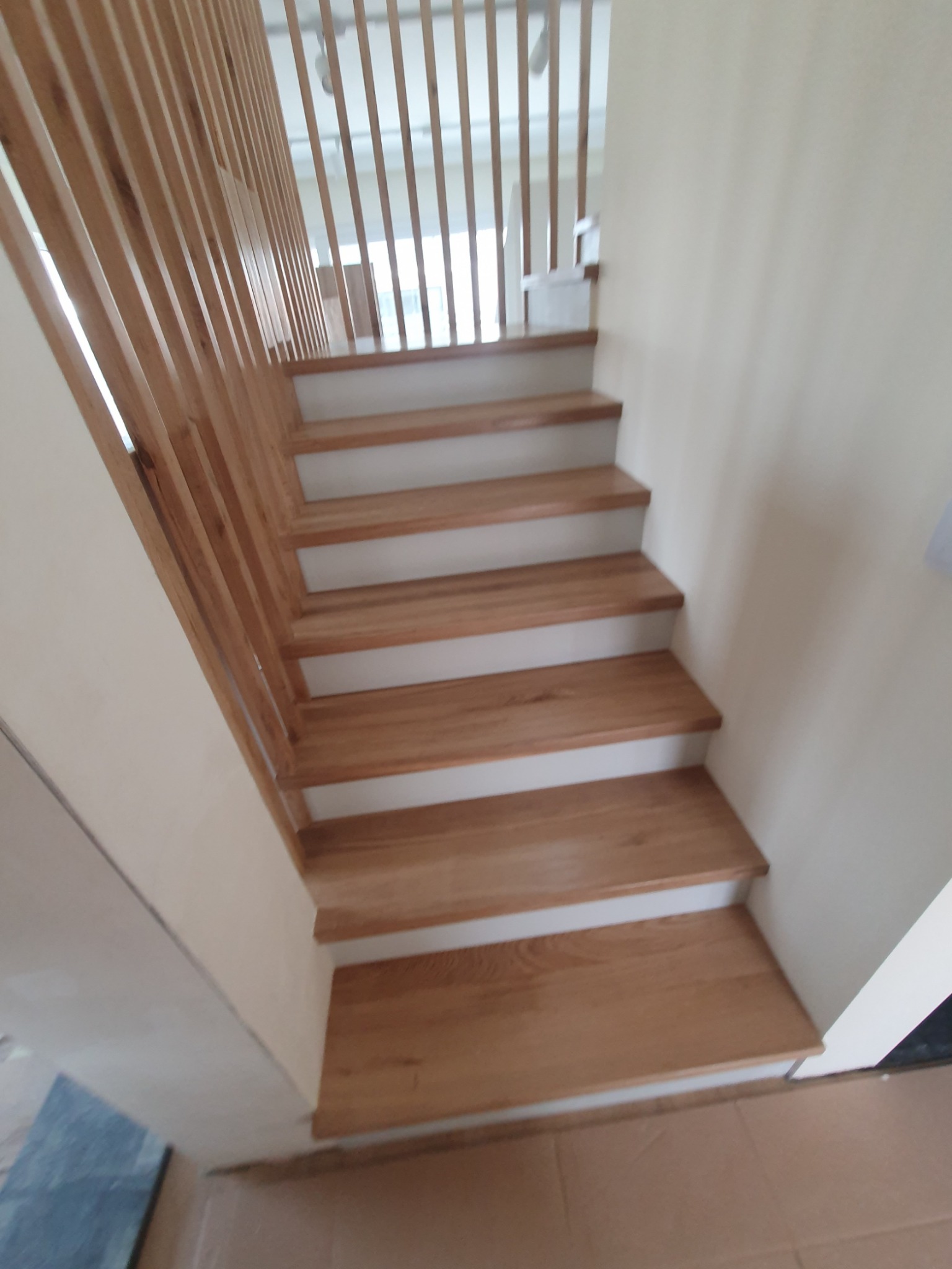 Nowoczesne schody z jasnego drewna z minimalistyczną, pionową balustradą, widok z dołu w górę.