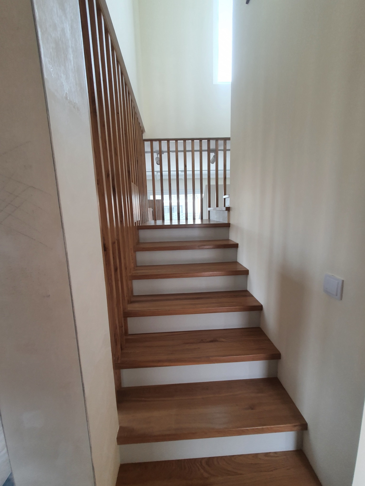 Jasne, drewniane schody z prostą, drewnianą balustradą w nowoczesnym wnętrzu, widok z dołu.