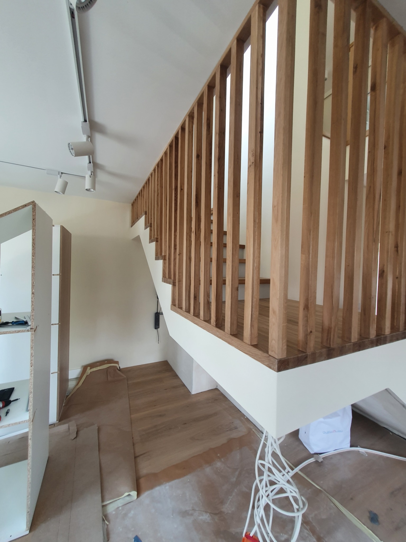 Montaż schodów z drewnianą balustradą w trakcie wykończenia wnętrza, widoczne elementy konstrukcyjne i przewody elektryczne.