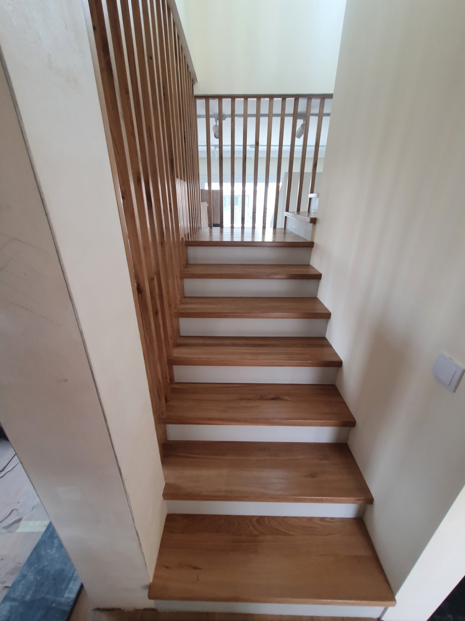 Jasne, drewniane schody z białymi podstopnicami i ażurową balustradą z pionowych listew, widok z dołu na górę.