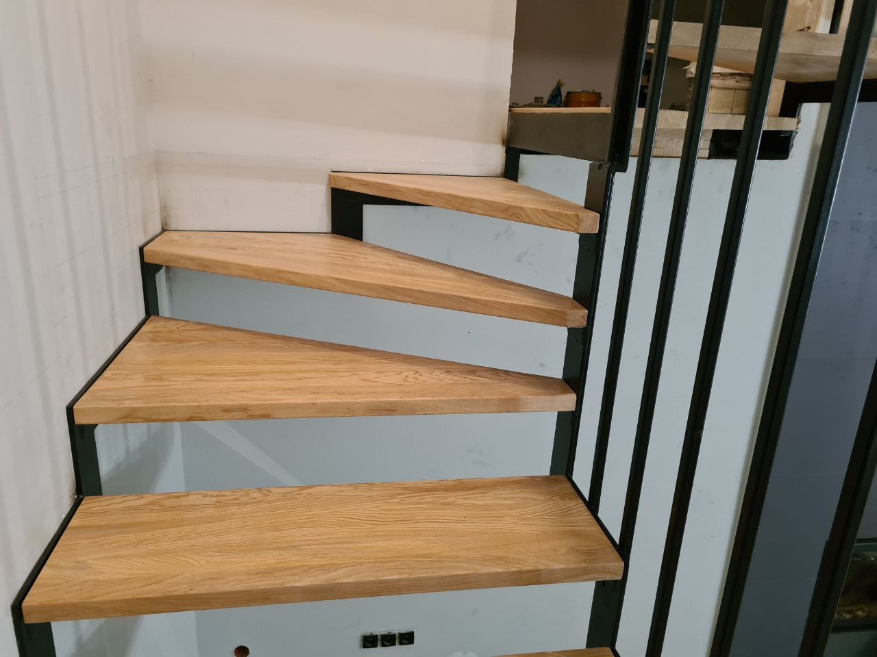 Schody drewniane z metalową konstrukcją i poręczą, widok z dołu na trzy stopnie o trójkątnym kształcie.