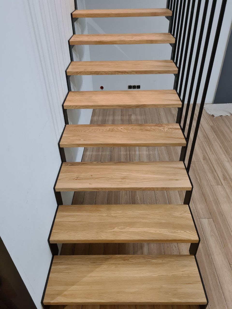 Stopnie z jasnego drewna z czarną metalową konstrukcją, widok z dołu, minimalistyczny design, jasne wnętrze.