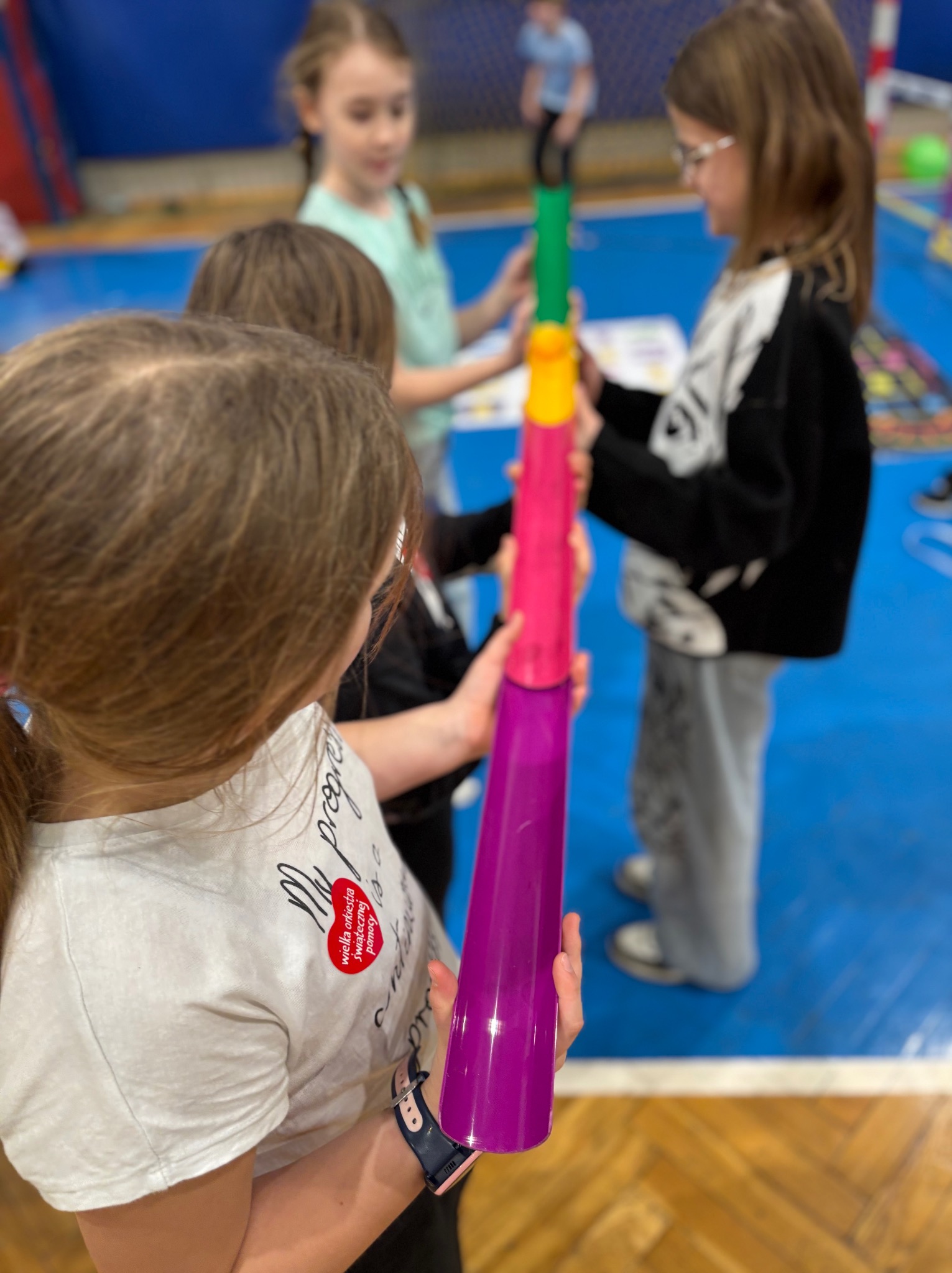 Dzieci w sali gimnastycznej podczas zabawy z kolorowymi, plastikowymi tubami, układając je w wieżę.