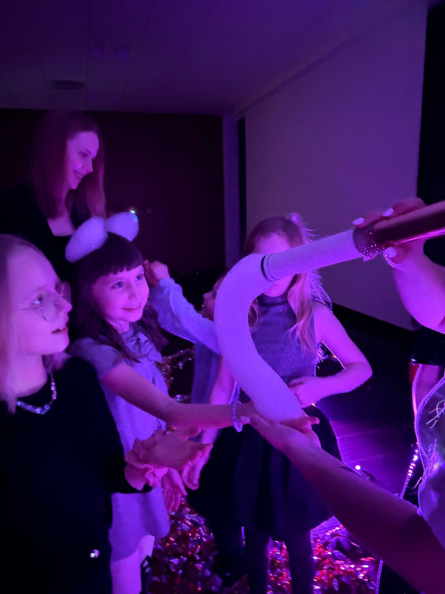 Dziewczynki w fioletowym świetle podczas pokazu z użyciem wytwornicy baniek mydlanych, na podłodze konfetti.