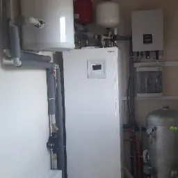 Pompa ciepła Hitachi oraz zbiorniki buforowe zainstalowane w pomieszczeniu technicznym w Pruszkowie, widoczne rury z izolacją termiczną i osprzęt.