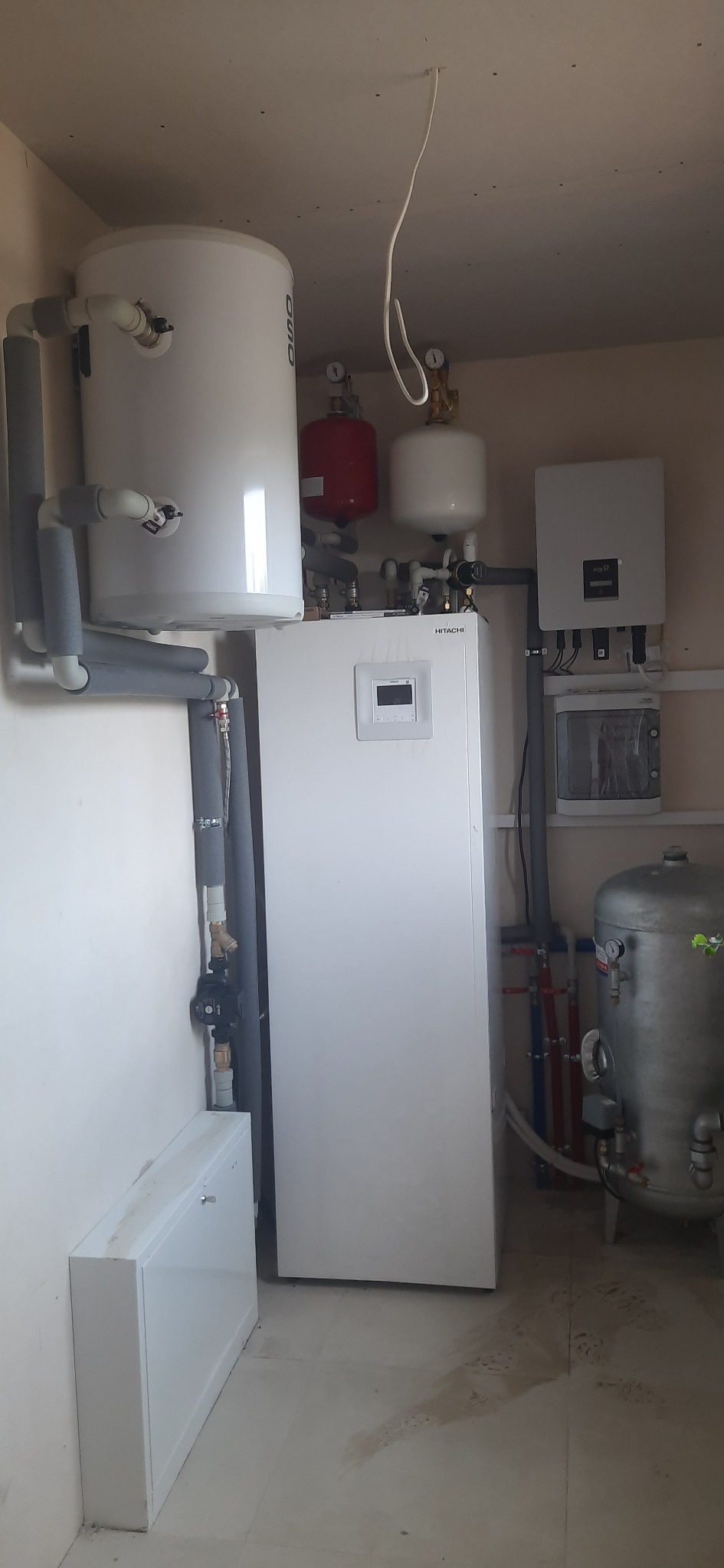 Pompa ciepła Hitachi oraz zbiorniki buforowe zainstalowane w pomieszczeniu technicznym w Pruszkowie, widoczne rury z izolacją termiczną i osprzęt.