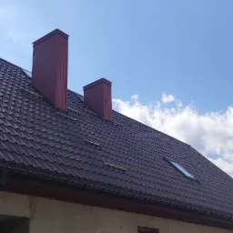 Nowy, brązowy dach z blachy trapezowej z dwoma kominami i oknem dachowym na tle błękitnego nieba z chmurami, Siedlce.