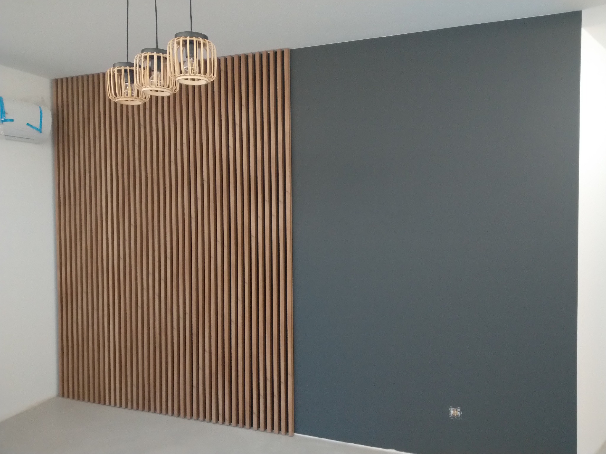Nowoczesne wnętrze z drewnianą ścianką działową z pionowych listew, pomalowaną szarą ścianą i trzema wiszącymi lampami z abażurami z naturalnego rattanu.