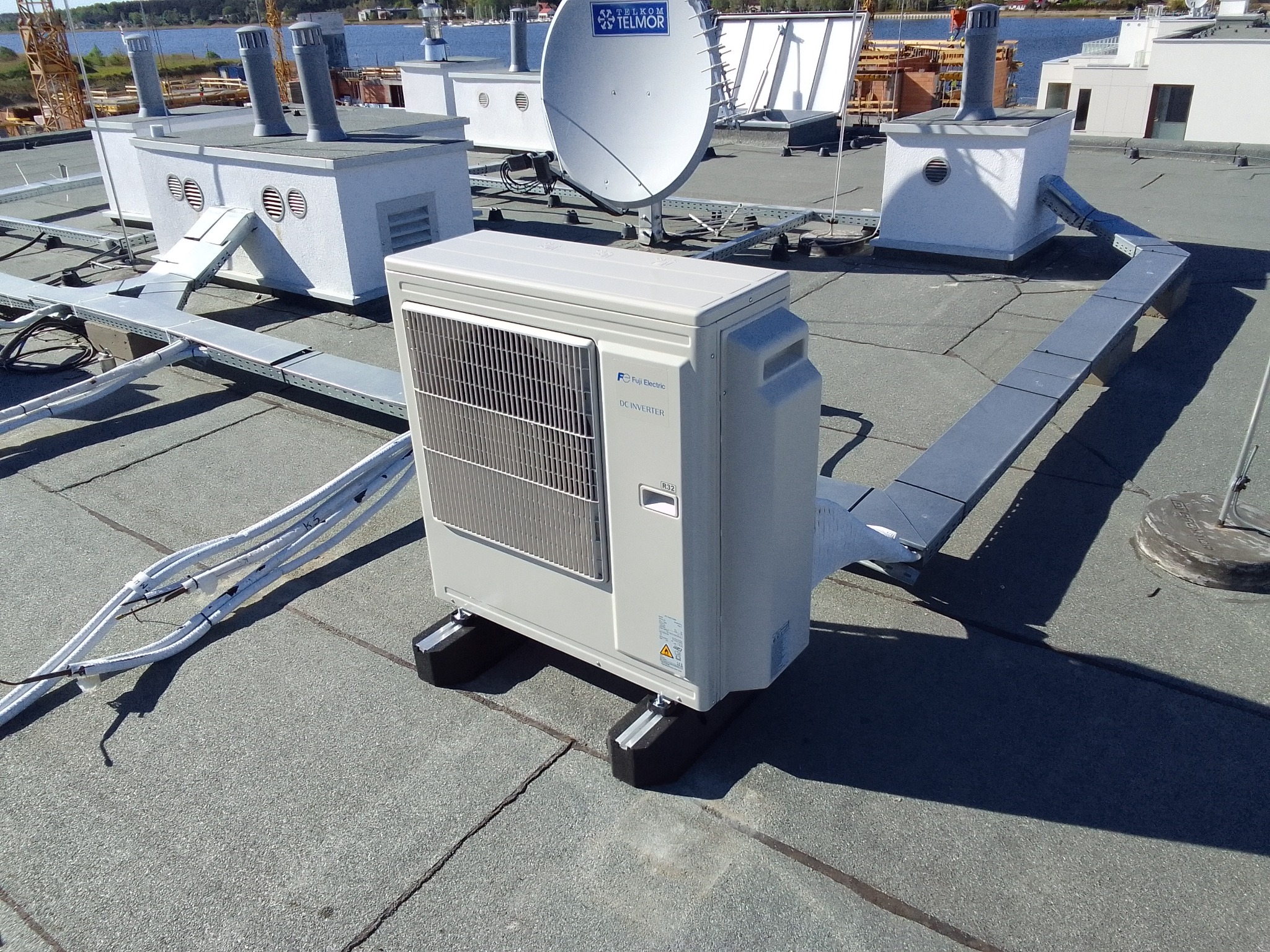 Agregat klimatyzacyjny Fuji Electric DC Inverter zamontowany na dachu budynku, z widocznymi przewodami, elementami wentylacyjnymi i anteną satelitarną w tle.
