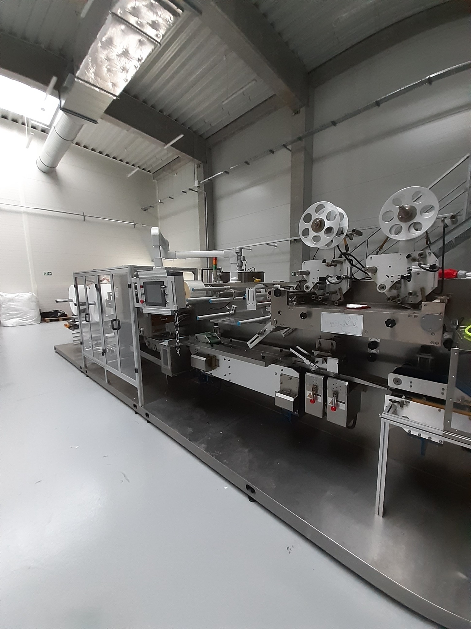 Automatyczna maszyna do pakowania w hali produkcyjnej, widoczne szpule z folią i panel sterowania.