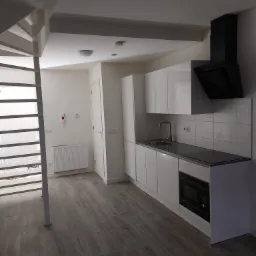 Nowoczesna, minimalistyczna kuchnia z białymi szafkami, czarnym okapem i szarą podłogą imitującą drewno; spiralne schody widoczne w tle.