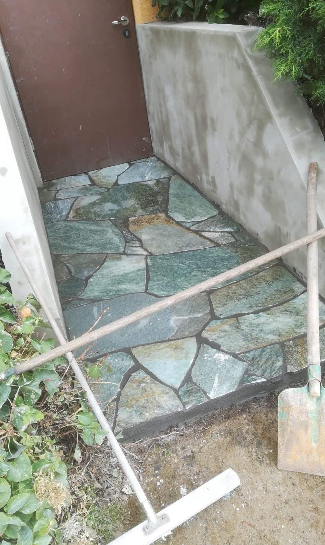 Wykończone wejście do budynku z nieregularnych, zielonych kamieni, widoczne narzędzia i świeżo otynkowana ściana.