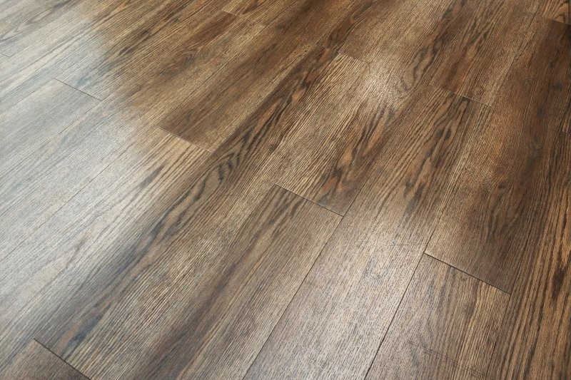 Ułożone panele podłogowe w odcieniach brązu z widoczną strukturą drewna, ułożone pod kątem, z delikatnym refleksem świetlnym.