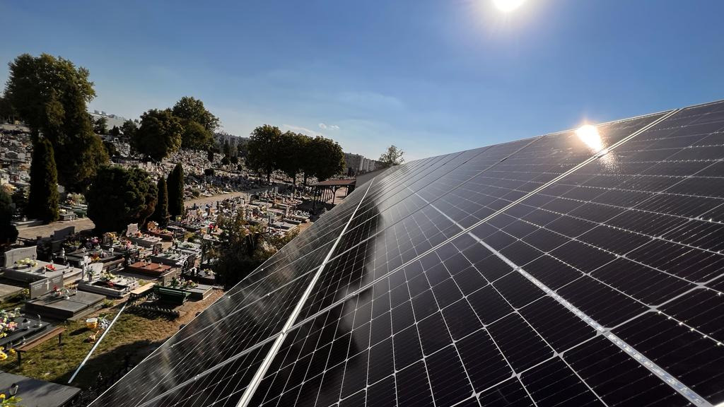 Panele słoneczne na dachu z widokiem na cmentarz w słoneczny dzień.