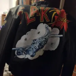 Czarna kurtka skórzana z ręcznie malowanym motywem bombowca B-17 w chmurach i napisem 'FLAK Lodge' nad nim, widok z tyłu.