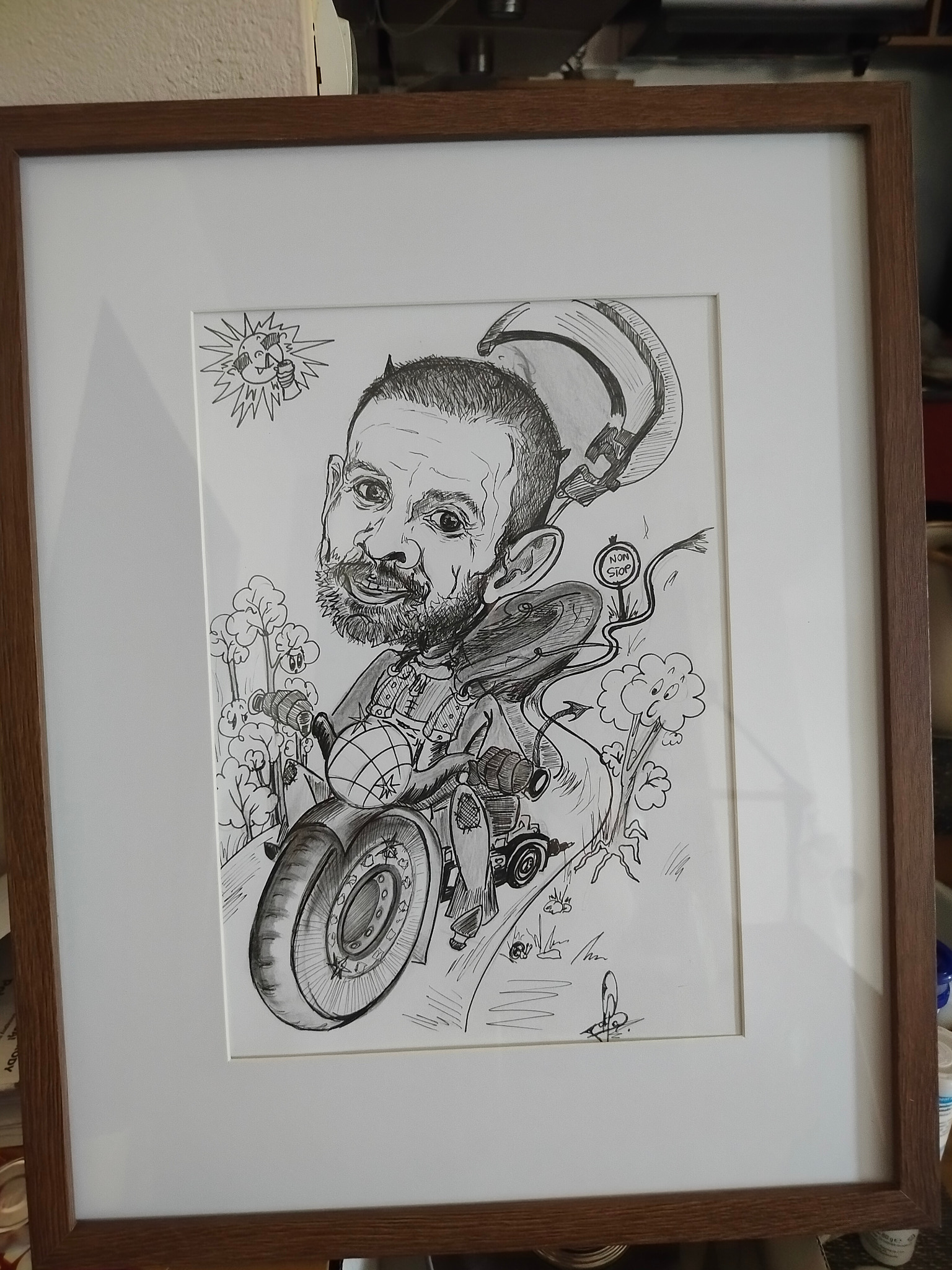Oprawiony w ramkę rysunek tuszem przedstawiający karykaturę brodatego mężczyzny na motocyklu, z elementami humorystycznymi jak słońce z zębami i drzewa z oczami, sygnowany w prawym dolnym rogu.