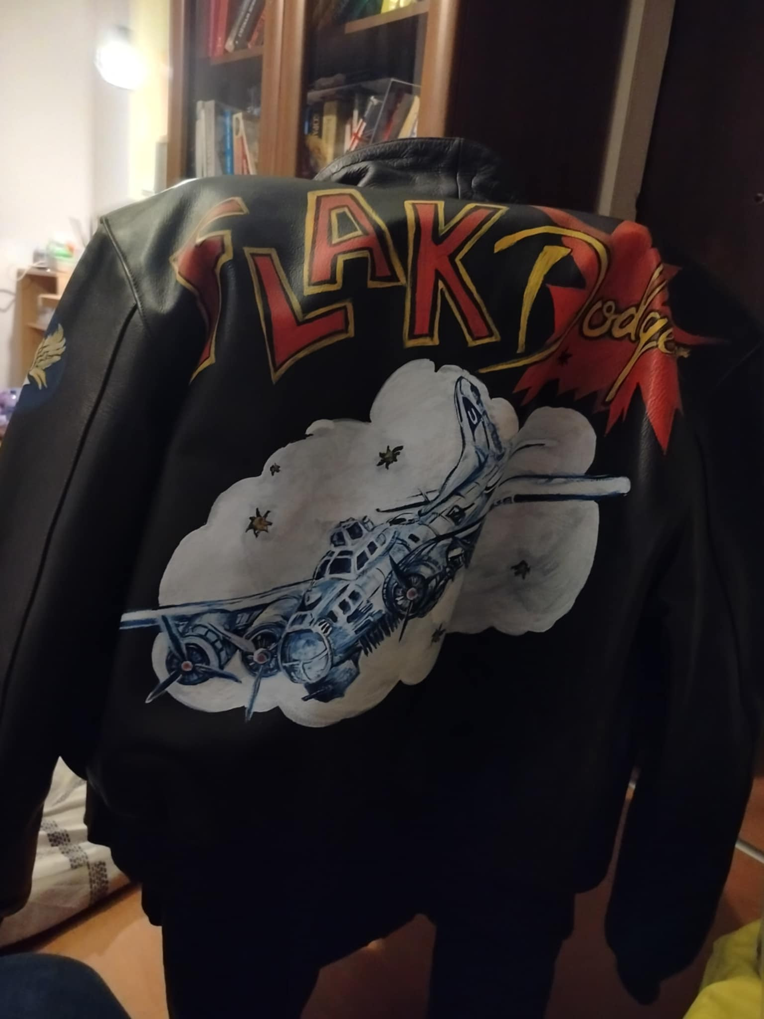 Czarna kurtka skórzana z ręcznie malowanym motywem bombowca B-17 w chmurach i napisem 'FLAK Lodge' nad nim, widok z tyłu.