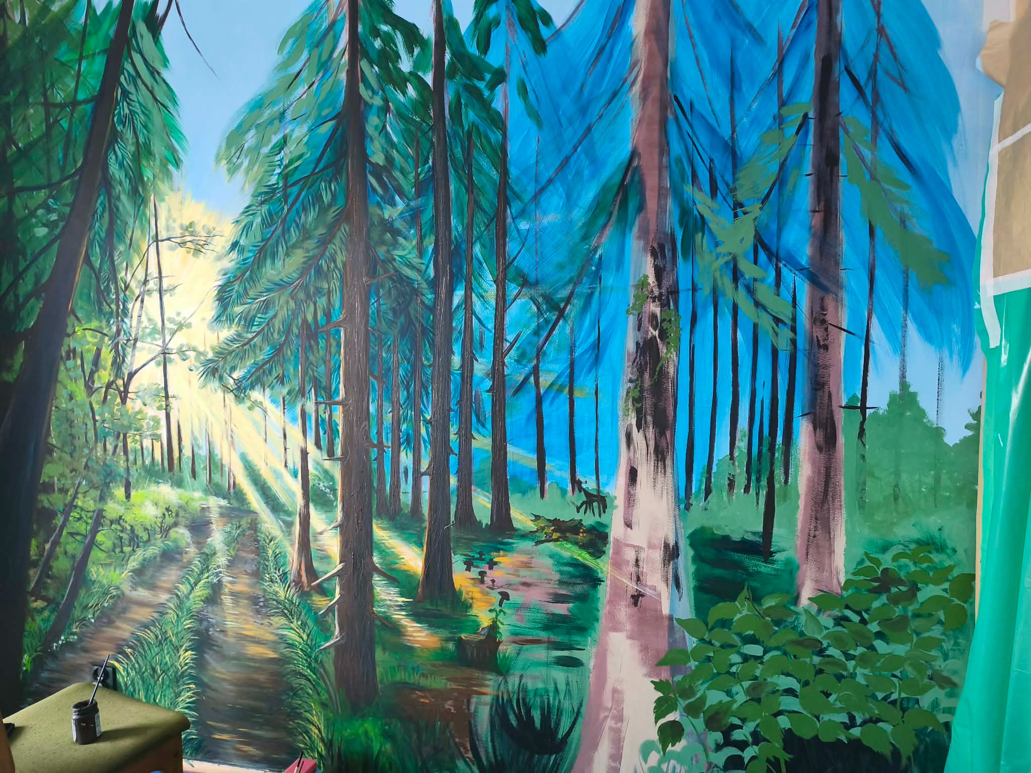 Niedokończony obraz leśnego krajobrazu z promieniami słońca, widoczne ślady pędzla i fragmenty niezamalowanej ściany, sugerujące etap tworzenia dzieła.