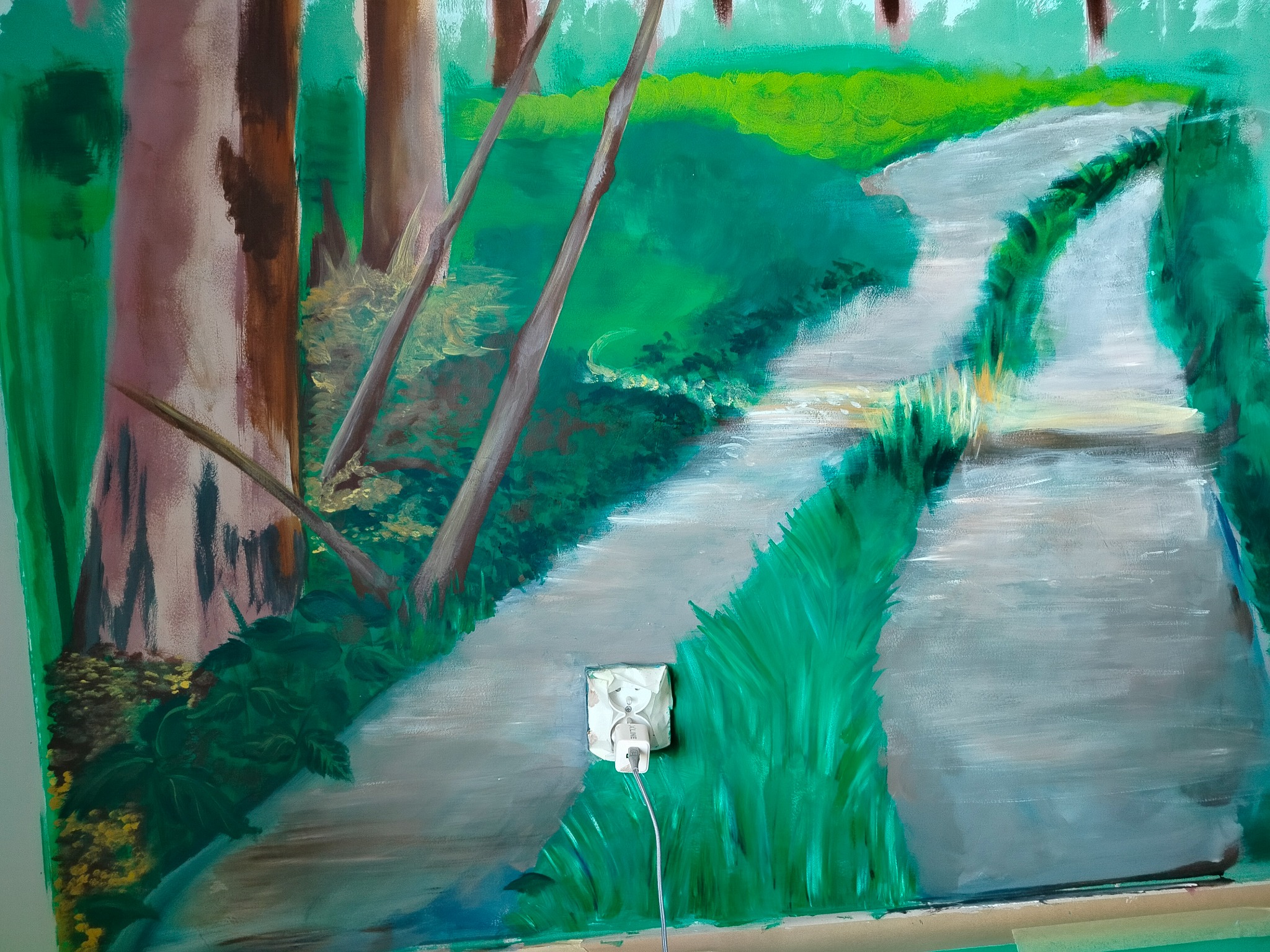 Niedokończony obraz olejny przedstawiający leśną ścieżkę z widocznym gniazdkiem elektrycznym i wtyczką, sugerujący malowanie na ścianie w pomieszczeniu.
