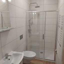 Huber Design - Nowoczesna łazienka we Wrocławiu z białymi płytkami, kabiną prysznicową z przesuwnymi drzwiami, umywalką z baterią oraz grzejnikiem drabinkowym.