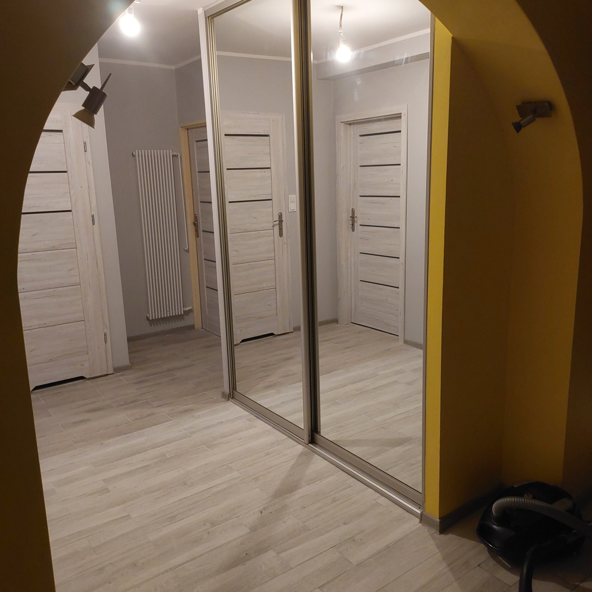 Dwudrzwiowa szafa przesuwna z lustrami w przedpokoju z beżową podłogą imitującą drewno i żółtą ścianą z łukowym przejściem