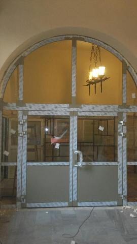 Arched doorway with newly installed double doors, visible framework and frosted glass panels, interior chandelier in background.