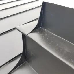 Szczeg&oacute;łowe ujęcie czarnej blachy na dachu z widocznymi obr&oacute;bkami blacharskimi, wykonane z bliska pod kątem.