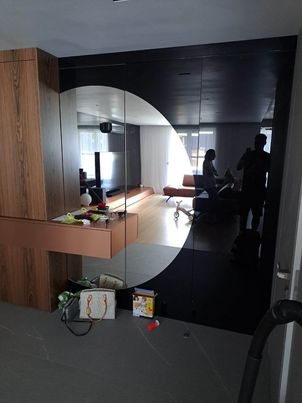 Czarne szklane panele ścienne z lustrzanym efektem odbijające wnętrze salonu, widoczne osobiste przedmioty na komodzie i podłodze.