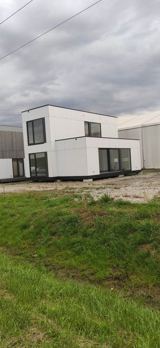 Nowoczesny, dwukondygnacyjny dom modułowy z dużymi oknami, ustawiony na trawie w pochmurny dzień.