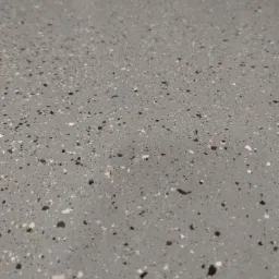 Szara, gładka powierzchnia z drobnymi, nieregularnymi plamkami w odcieniach bieli i czerni, przypominająca lastryko.