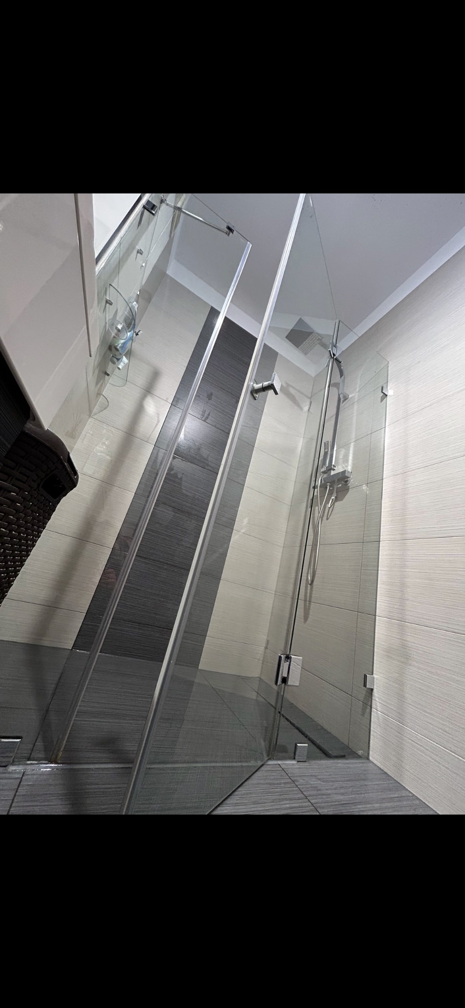 Szklana kabina prysznicowa z chromowanymi okuciami i deszczownicą, wyłożona płytkami w odcieniach szarości i beżu.