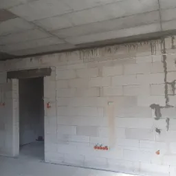 Surowy stan wnętrza z widocznymi przewodami elektrycznymi poprowadzonymi po ścianach z betonu komórkowego, pomarańczowe puszki instalacyjne rozmieszczone w różnych punktach pomieszczenia, widoczne...