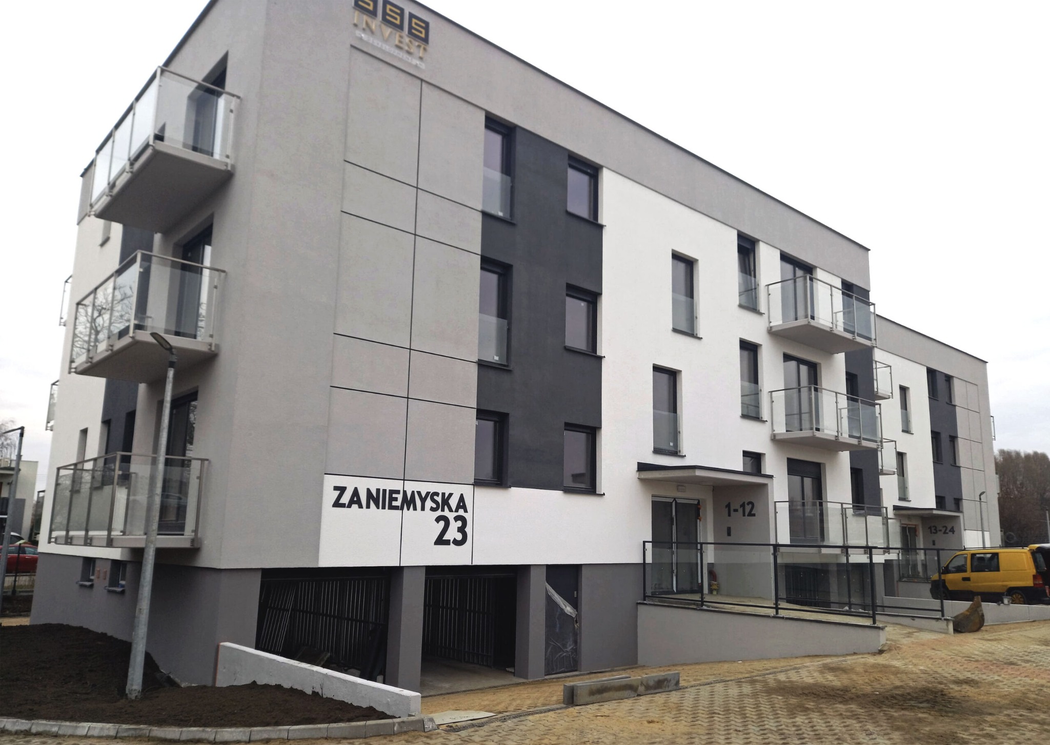 Nowoczesny budynek mieszkalny z balkonami, elewacją w odcieniach szarości i bieli, widoczny adres 'Zaniemyska 23' oraz żółty samochód dostawczy w tle.