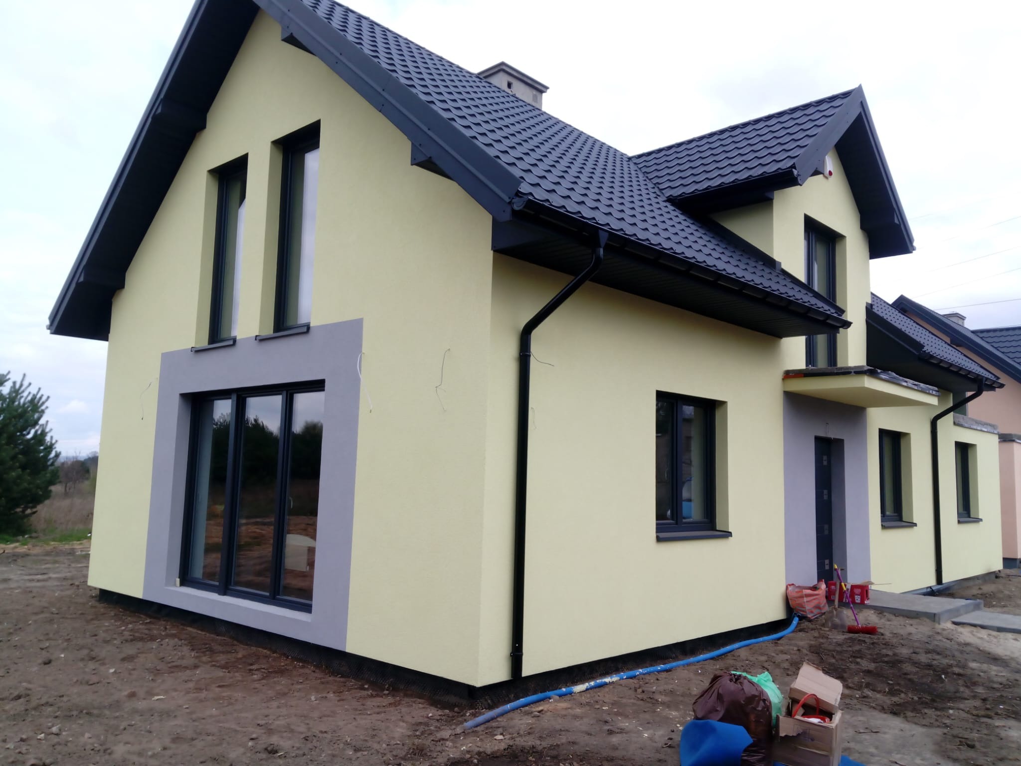 Nowoczesny dom jednorodzinny w Pińczowie z żółtą elewacją i antracytowym dachem, widoczne detale wykończenia, teren wokół domu w trakcie zagospodarowywania.