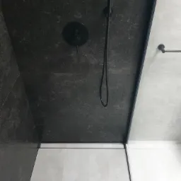 Nowoczesna kabina prysznicowa z ciemnoszarą płytką na ścianach i suficie, czarna armatura, odpływ liniowy i jasne płytki podłogowe.