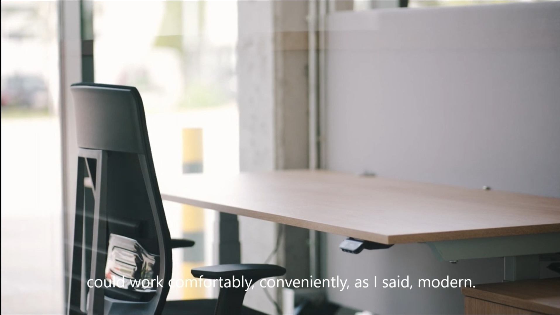 Nowoczesne biuro z regulowanym biurkiem i ergonomicznym krzesłem, widok z boku, jasne wnętrze.