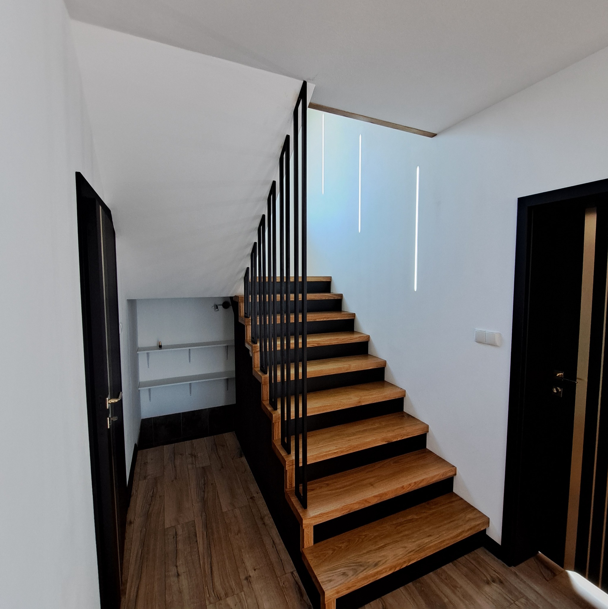 Nowoczesne schody drewniane z czarną, minimalistyczną balustradą w jasnym wnętrzu z oświetleniem LED.