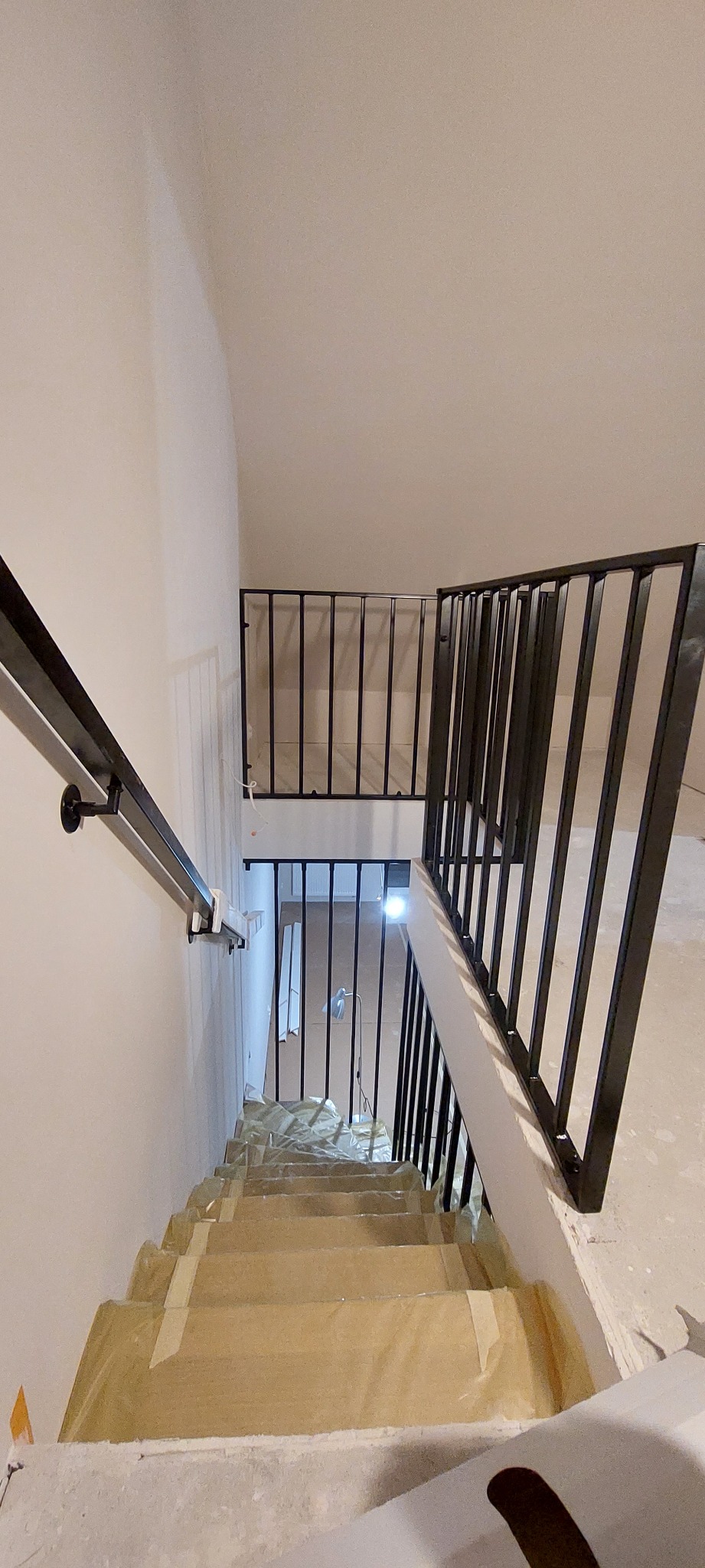 Metalowa balustrada schodowa w trakcie montażu, zabezpieczone schody folią, widok z góry.