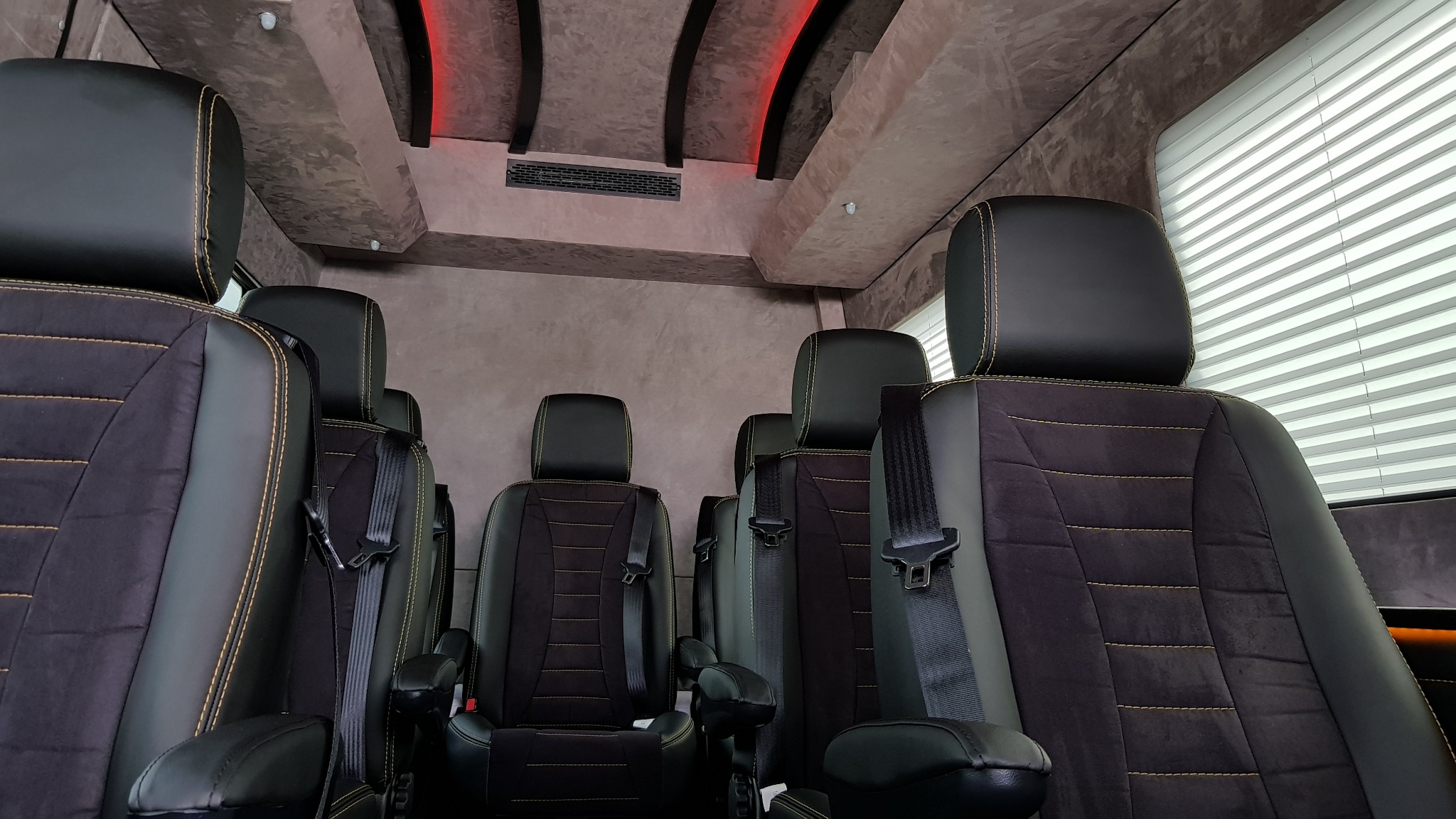 Wnętrze luksusowego busa z czarnymi skórzanymi fotelami z żółtymi przeszyciami, widok na kilka rzędów siedzeń, klimatyzacja i oświetlenie ambientowe.