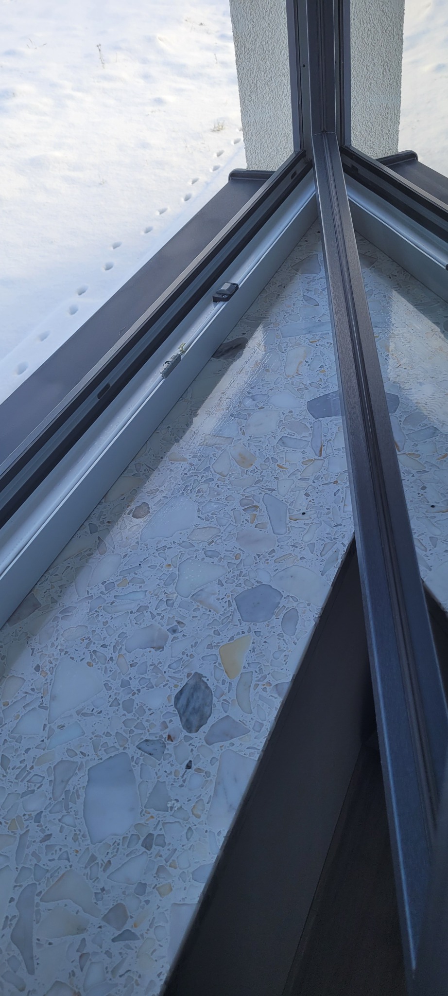 Wnętrze okna narożnego z widokiem na zaśnieżony teren, widoczne ślady zwierząt na śniegu, parapet wykończony mozaiką.