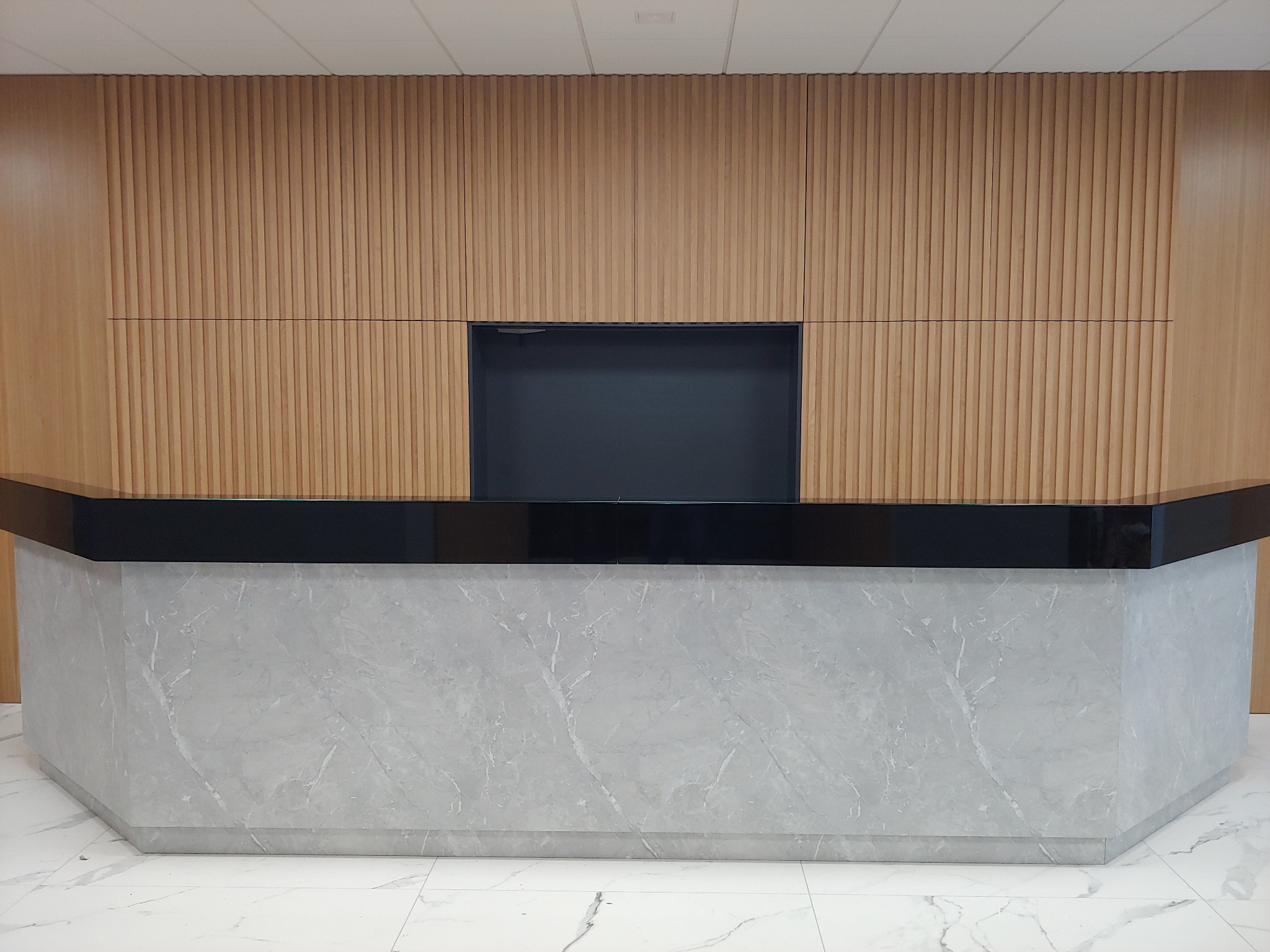 Recepcja biurowa z marmurowym blatem i drewnianą ścianą z lamelami, widok z przodu.
