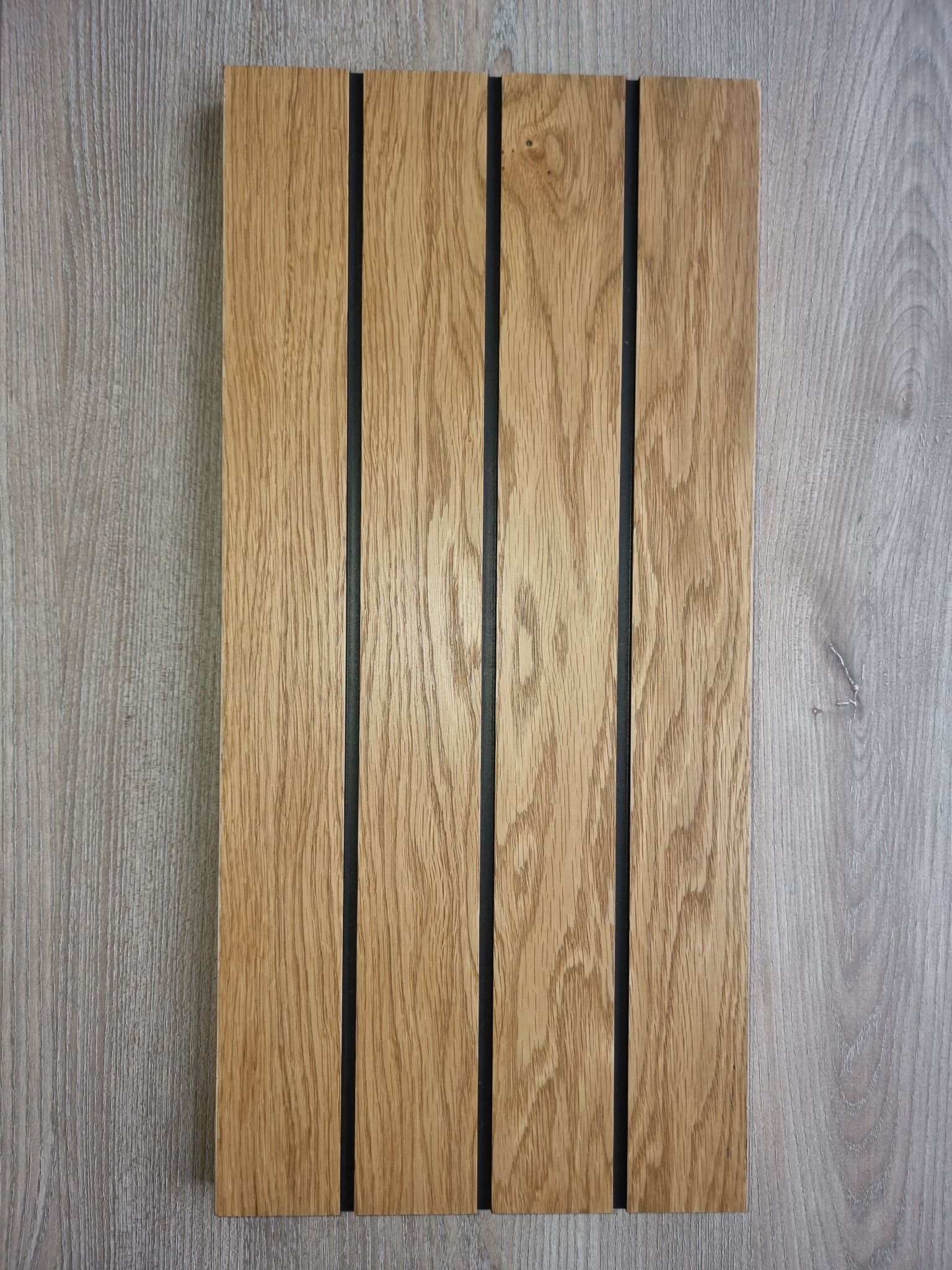 Panel z jasnego drewna dębowego z trzema czarnymi, pionowymi wstawkami, ułożony na tle imitującym drewno o szarym odcieniu.