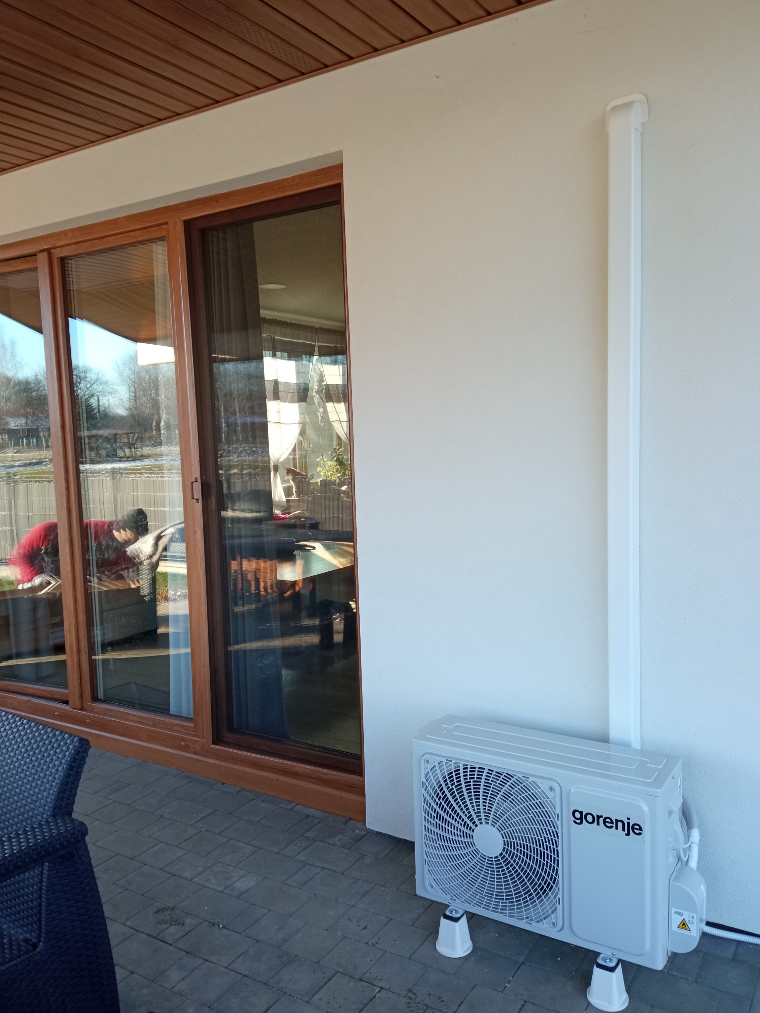 Zewnętrzna jednostka klimatyzacji Gorenje zamontowana na tarasie domu, z widoczną instalacją odprowadzającą skropliny i osłoną przewodów na ścianie.
