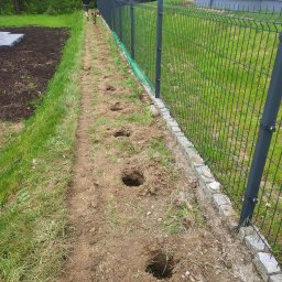 Hermes GardenBud - Przygotowanie terenu pod montaż ogrodzenia panelowego: wykopane dołki wzdłuż obrzeża z kostki granitowej, widoczny fragment zamontowanego ogrodzenia i osoba z glebogryzarką.