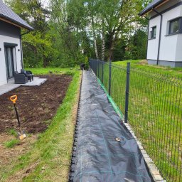 Hermes GardenBud - Przygotowanie terenu pod ogród: rozłożona agrowłóknina z siatką, obok świeżo przekopana ziemia i szpadel. W tle widoczny fragment ogrodzenia panelowego.